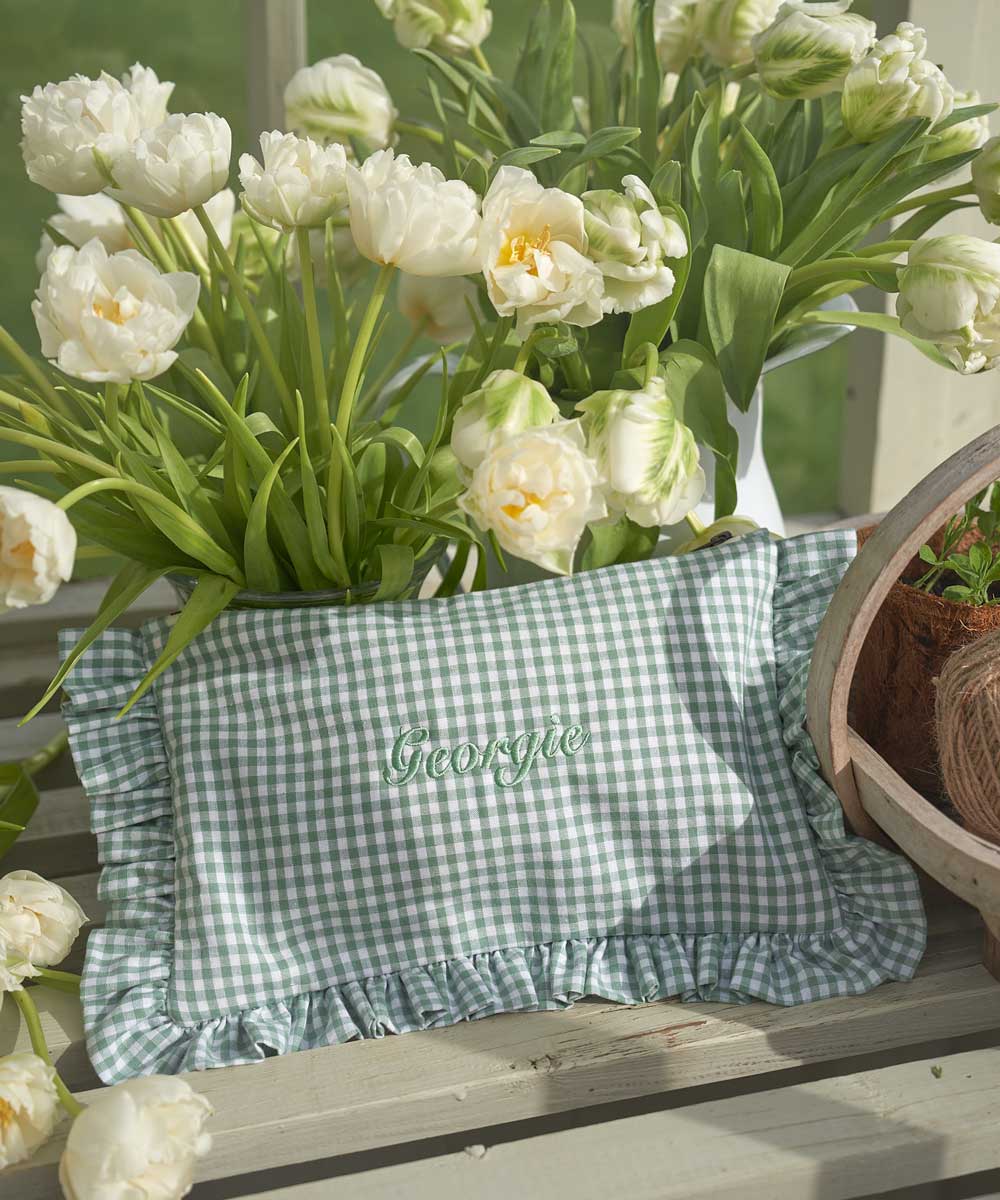 Green checkered ruffled pouch with 'Georgia' embroidery surrounded by white tulips on a wooden surface.