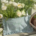 Green checkered ruffled pouch with 'Georgia' embroidery surrounded by white tulips on a wooden surface.