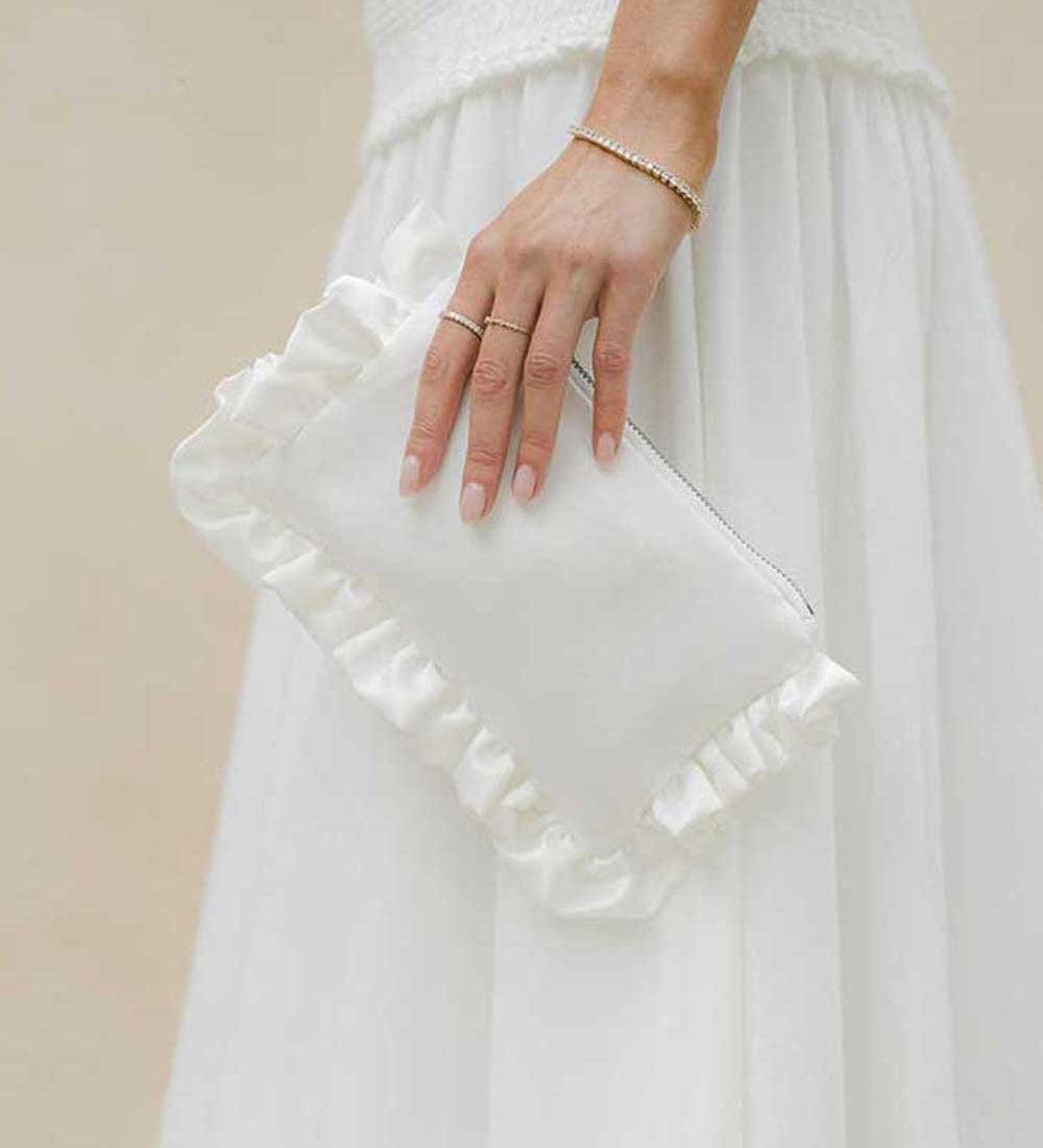 ivory ruffled clutch held by a person wearing a white dress against a beige background