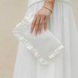 ivory ruffled clutch held by a person wearing a white dress against a beige background