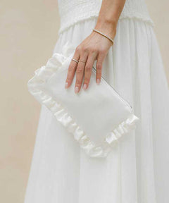 ivory ruffled clutch held by a person wearing a white dress against a beige background