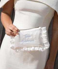 White clutch with 'Just Married' embroidery held by a person in a white dress.