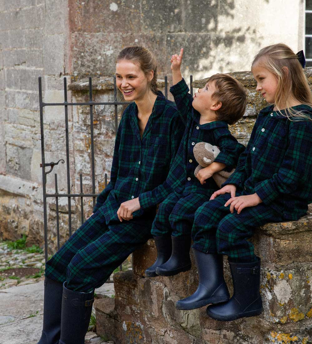 Family of three wearing matching black watch plaid pyjamas sitting on stone steps.