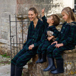 Family of three wearing matching black watch plaid pyjamas sitting on stone steps.