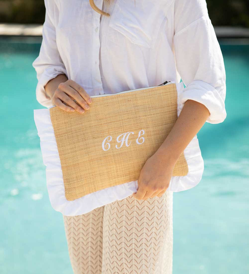 Person holding a straw clutch embroidered with initials by a pool