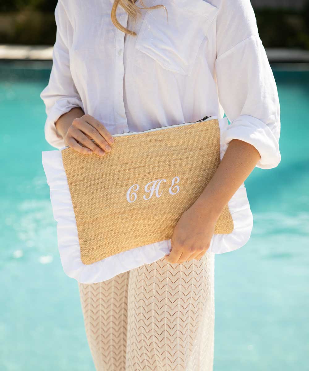 Person holding a straw clutch embroidered with initials by a pool