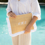 Person holding a straw clutch embroidered with initials by a pool