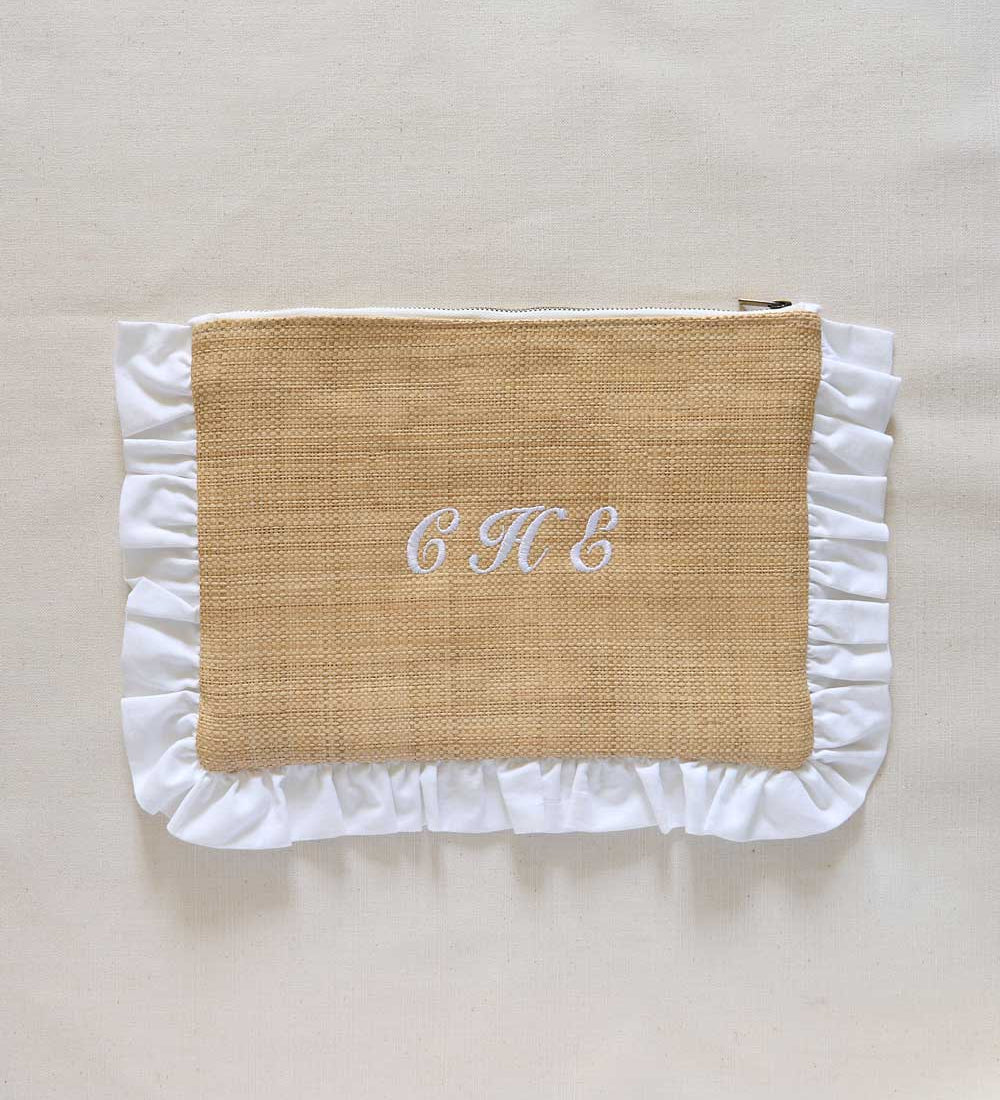 Raffia textured pouch with white ruffled edges and initials 'C H E' on a beige background