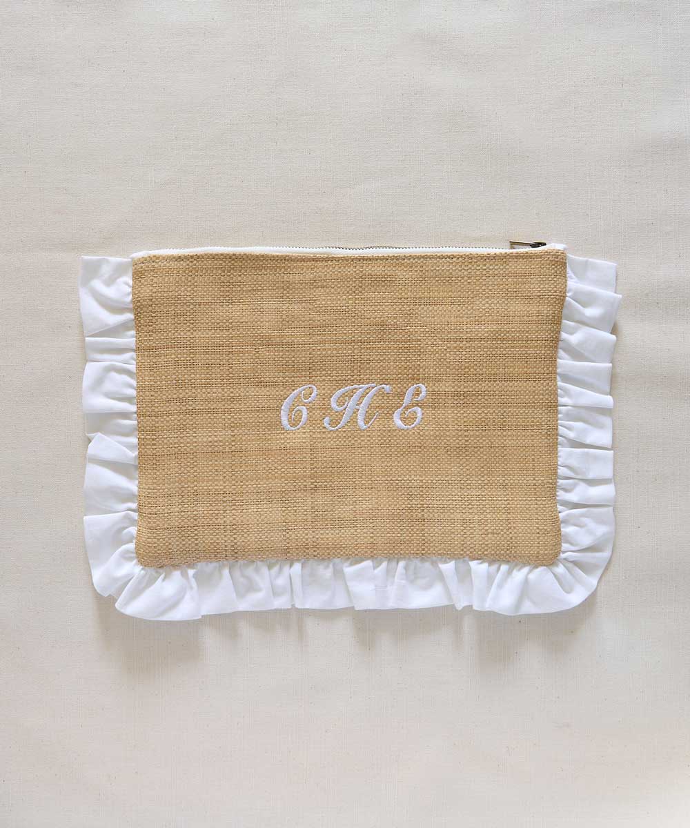 Raffia textured pouch with white ruffled edges and initials 'C H E' on a beige background