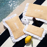 Three woven bags with white ruffle edges on a black and white striped surface near water.