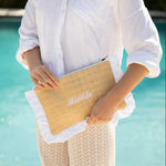 person holding straw pouch with white ruffles and a name embroidered 